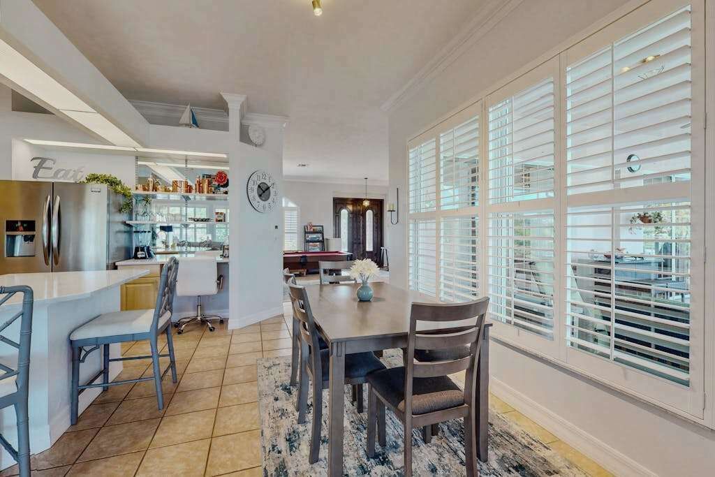 A modern kitchen with a dining area, a refrigerator, and a clock on the wall.