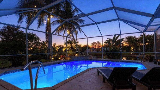 A swimming pool with lounge chairs, a covered area, and palm trees. - Canal-Front Home with Private Pool and Dock, WiFi, and Pool Table (Cape Coral)