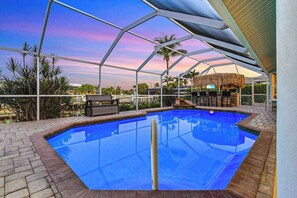A swimming pool with a glass enclosure, surrounded by a patio area with seating and a bar. - Wonderful oasis w/lanai, private pool, tropical bar, private dock, Gulf access (Cape Coral)