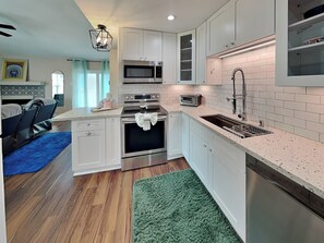 A modern kitchen with white cabinetry, stainless steel appliances, and a green rug. - Palms at Cove View 612 | Beach Views + Community Pool! (Galveston)