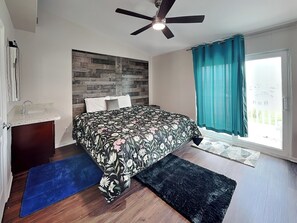 A bedroom with a bed, a ceiling fan, a window with curtains, a wooden headboard, and a small bedside table. - Palms at Cove View 612 | Beach Views + Community Pool! (Galveston)
