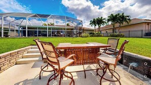 Un patio con mesa y sillas, un área exterior cubierta y un césped con un edificio al fondo.