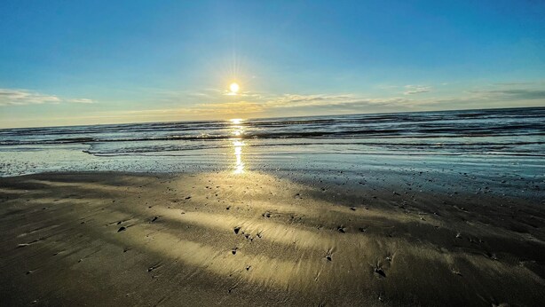 Une plage où le soleil se reflète sur le sable mouillé, créant un chemin de lumière.