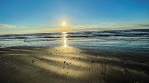 A beach with the sun reflecting on the wet sand, creating a path of light. - Ocean Outlook | Spacious Home + Community Pool (Port Aransas)