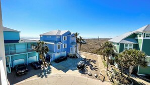Une maison à deux étages, avec une façade bleue, un allée couverte et une vue sur la plage.