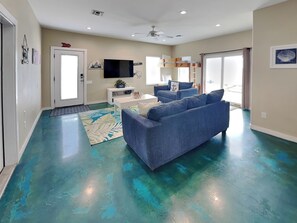 Ein Wohnzimmer mit einem blauen Sofa, einem weißen Couchtisch, einem Flachbildfernseher und einem Deckenventilator.