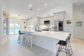 A modern kitchen with white cabinetry, a large island, bar stools, and a view to the outside. - Waterfront dream - heated infinity pool & therapeutic spa, sunset views & office (Cape Coral)