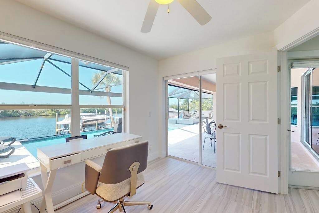 Una habitación con escritorio, silla, ventanas amplias y una puerta que da a un balcón con vista a la piscina.