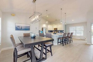 A modern kitchen with a central island, pendant lighting, and a dining area with a dark wooden table and chairs. - Newly remodeled home with private pool and pool spa, gas grill, & W/D - dogs ok (Cape Coral)
