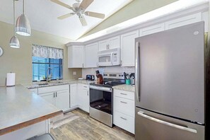 A modern kitchen with white cabinets, stainless steel appliances, a ceiling fan, and a window with a view. - Cozy home with private pool. internet, & washer and dryer (Cape Coral)
