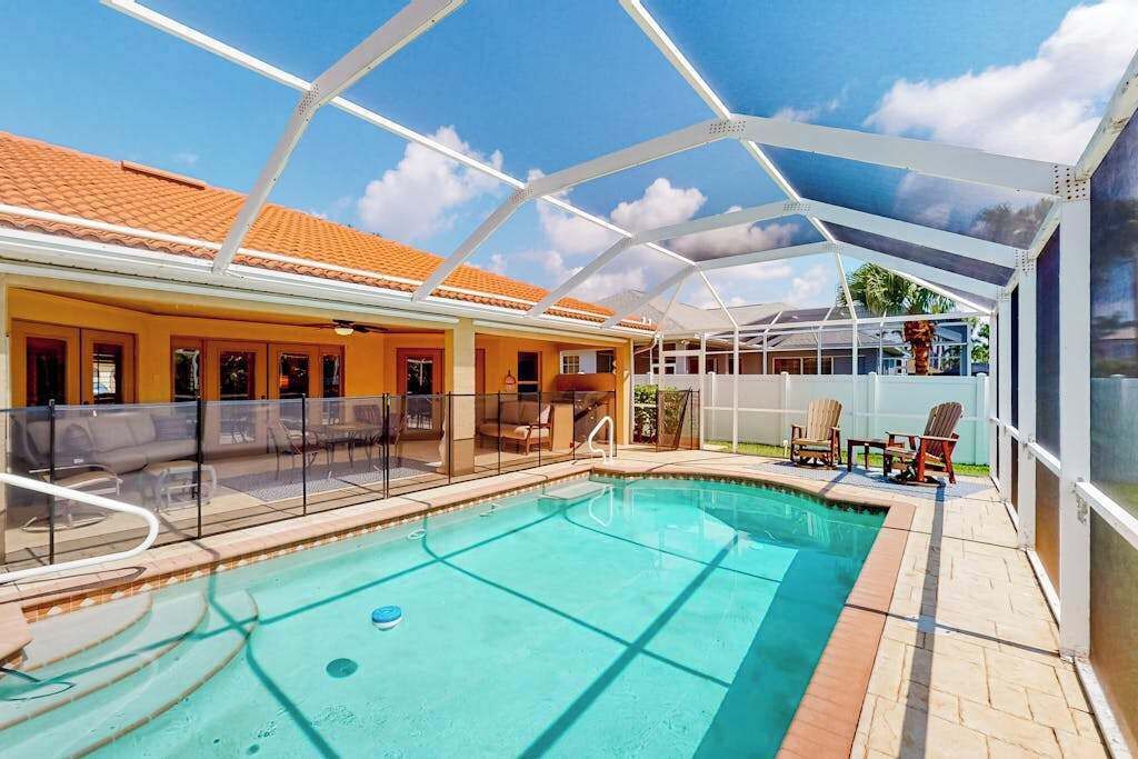 A pool area with a covered patio, outdoor seating, and a view of a building with a tiled roof.