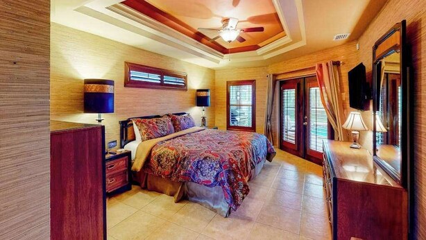 A bedroom with a large bed, a ceiling fan, a TV, and a window with curtains. - Inviting home with pool, water view, enclosed yard, central AC, W/D (Cape Coral)