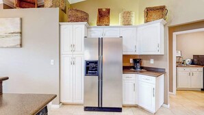 A kitchen with white cabinets, a stainless steel refrigerator, and wicker baskets on the upper cabinets. - Inviting home with pool, water view, enclosed yard, central AC, W/D (Cape Coral)