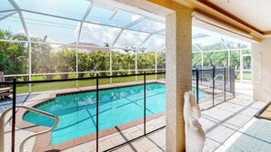A swimming pool with a glass enclosure, a statue, and a view of greenery outside. - Inviting home with pool, water view, enclosed yard, central AC, W/D (Cape Coral)