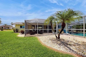 A covered outdoor area with a pool, palm tree, and a patio with outdoor furniture. - Canal-front home with screened pool, dock access, patio, grill, AC, & W/D (Cape Coral)