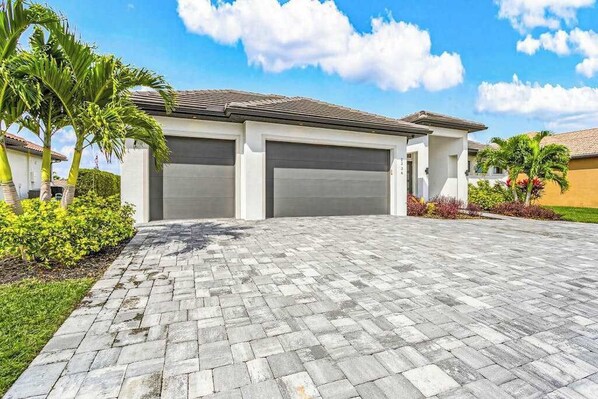 A residential building with two garage doors, a paved driveway, and palm trees. - Stunning Canalfront Escape with Infinity Pool (Cape Coral)