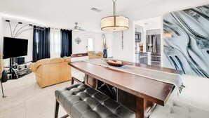 Una sala de estar moderna con un televisor de pantalla plana grande, un sofá, una mesa de comedor y una cocina al fondo.