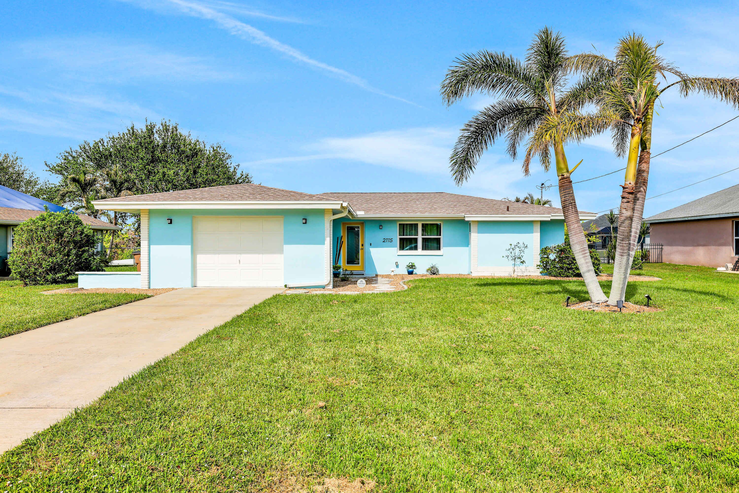 A single-story house with a front garage, a well-maintained lawn, and two palm trees.