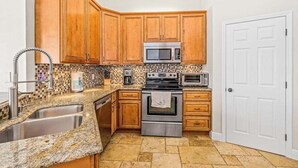 Eine Küche mit Holzausstattung, einem Edelstahlspülbecken, einer Mikrowelle, einem Backofen und einer gefliesten Spritzschutzwand.