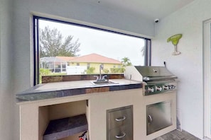 Eine kleine Küche mit integriertem Grill, einem Fenster mit Blick auf eine Wohngegend und einem Spülbecken.