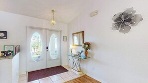 A hallway with a white door, a glass console table with a lamp, and a wall decoration. - Spacious Lakefront Home with a Screened-In Pool in Exclusive Community (Fort Myers)