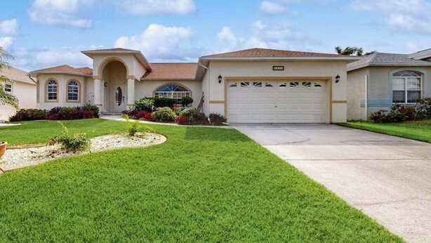 A residential house with a garage, a well-maintained lawn, and a clear sky. - Spacious Lakefront Home with a Screened-In Pool in Exclusive Community (Fort Myers)