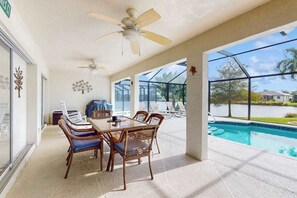 Eine überdachte Terrasse mit Pool, Gartenmöbeln und Deckenventilatoren.