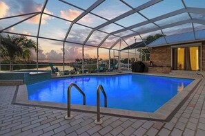 A swimming pool with a glass enclosure, surrounded by lounge chairs and a brick patio. - Exquisite waterfront home with private pool, hot tub, amd dock (Cape Coral)