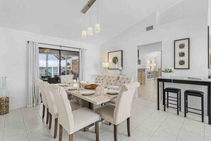 A spacious dining area with a large table and chairs, a kitchen area with a bar, and a view through a glass door. - Exquisite waterfront home with private pool, hot tub, amd dock (Cape Coral)
