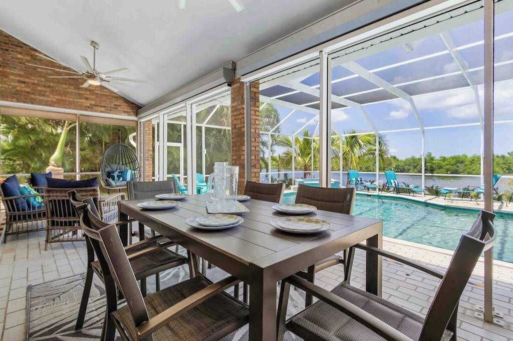 A covered dining area with a pool view, large windows, and outdoor seating.