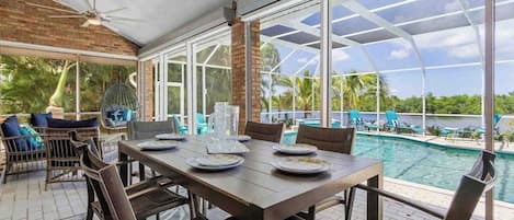 A covered dining area with a pool view, large windows, and outdoor seating.