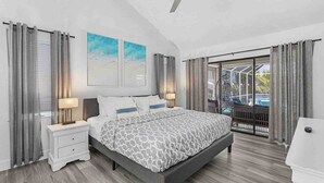 Quarto com cama, mesas de cabeceira, ventoinha no teto e varanda com cortinas.