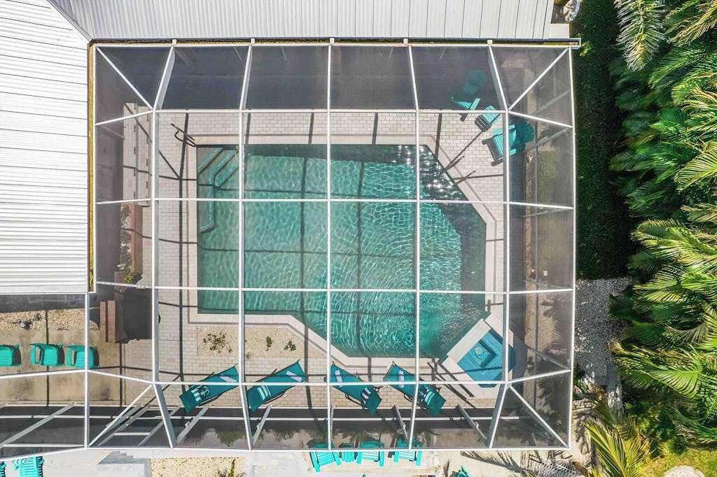 Une piscine dotée d’une structure en verre aux formes géométriques, entourée de verdure et d’un bâtiment.