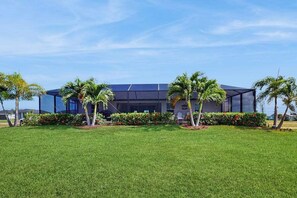 A modern building with a flat roof, surrounded by a well-maintained lawn and palm trees. - Quiet home with private pool, hot tub, and plenty of outside space (Cape Coral)