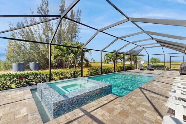 A covered outdoor swimming pool with a glass bottom, surrounded by a metal frame, and a patio area with lounge chairs. - Quiet home with private pool, hot tub, and plenty of outside space (Cape Coral)