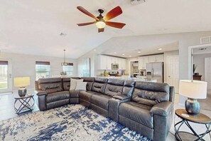 A living room with a sectional sofa, a ceiling fan, and a kitchen in the background. - Quiet home with private pool, hot tub, and plenty of outside space (Cape Coral)