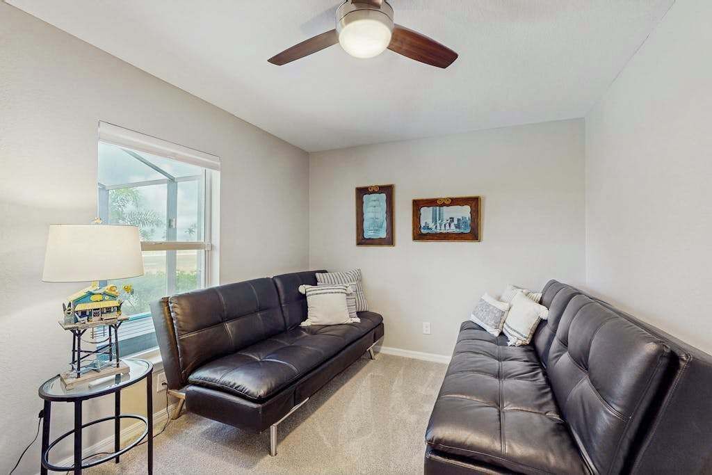A living room with two black leather sofas, a small side table with a lamp, and a ceiling fan.