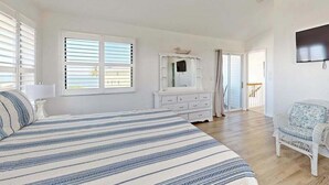 Et soveværelse med seng, kommode, stol og ventilator.