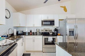 A modern kitchen with white cabinets, a stainless steel refrigerator, a microwave, an oven, and a clock on the wall. - Cozy Home with backyard, canal view, fully equipped kitchen, dog friendly (Cape Coral)