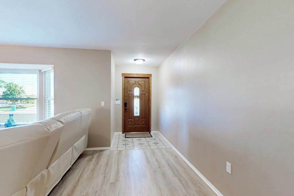 Un pasillo con una puerta de madera, una ventana con persianas y una pared color beige.