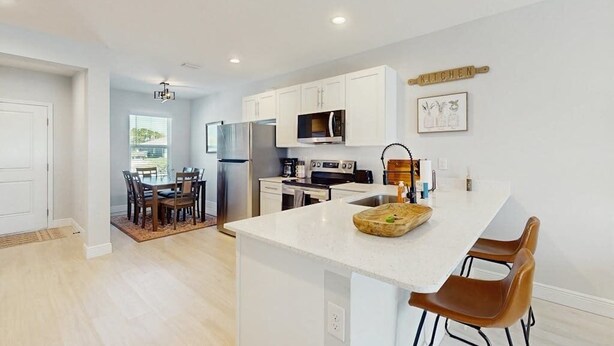 A modern kitchen with white cabinets, a central island, and a dining area with a table and chairs. - Coastal duplex with internet, washer and dryer, and dog friendly (Englewood)
