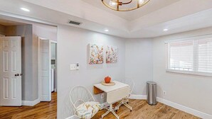 Una habitación con una mesa blanca, dos sillas, una lámpara en el techo y una ventana con persianas.