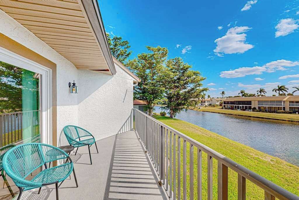 A balcony with chairs, a railing, and a view of a water body and buildings.