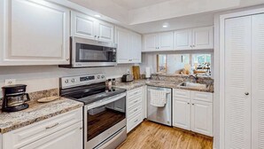 Cocina moderna con armarios blancos, horno empotrado, microondas y encimera de granito.