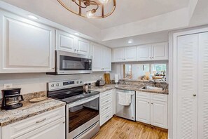 A modern kitchen with white cabinets, a built-in oven, a microwave, and a granite countertop. - Waterfront condo with balcony, pool, pickball/tennis, & walking paths (Fort Myers)