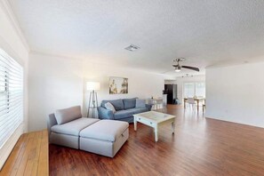 A spacious living room with a sofa, ottoman, coffee table, and a dining area with chairs and a table. - Bright and airy home with enclosed pool, hammock, and open-concept interior (Fort Myers)