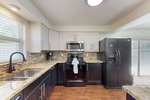 A modern kitchen with a granite countertop, stainless steel appliances, and dark cabinetry. - Bright and airy home with enclosed pool, hammock, and open-concept interior (Fort Myers)
