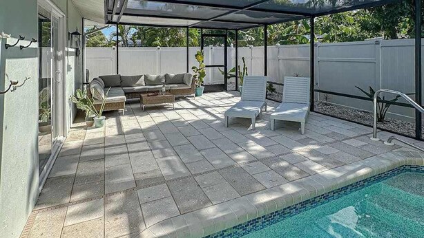 A covered outdoor area with a pool, a sofa, and two lounge chairs. - Bright and airy home with enclosed pool, hammock, and open-concept interior (Fort Myers)