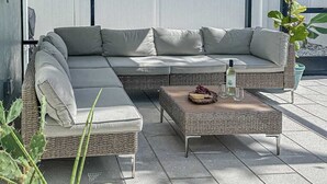 A wicker sectional sofa with cushions, a wicker coffee table with a bottle and fruit, and a potted plant. - Bright and airy home with enclosed pool, hammock, and open-concept interior (Fort Myers)