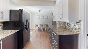 A kitchen with dark cabinets, a black refrigerator, a granite countertop, and a dining area with a table and chairs. - Bright and airy home with enclosed pool, hammock, and open-concept interior (Fort Myers)